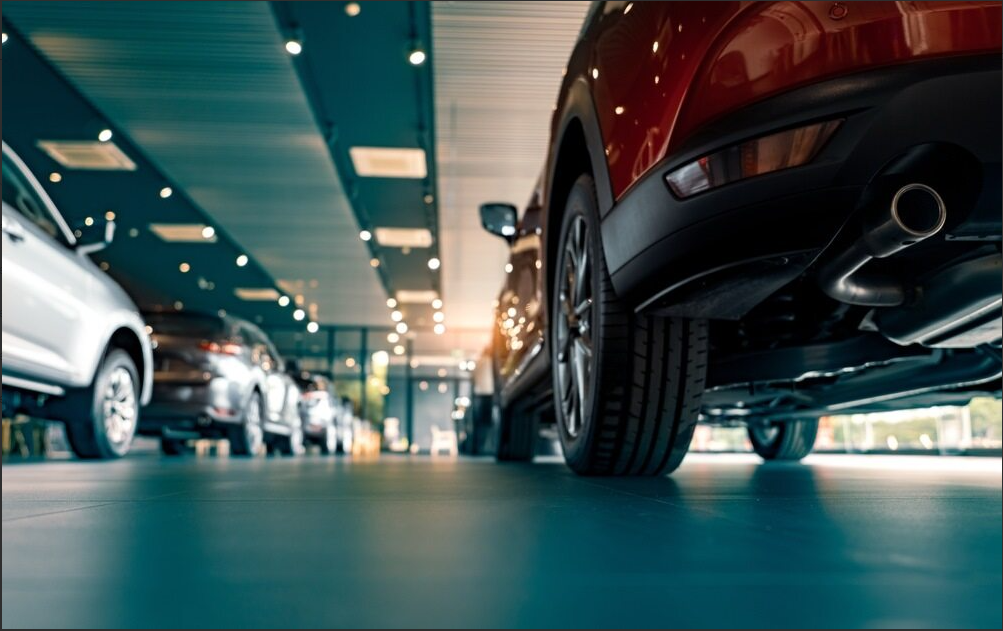 A photo taken from a long angle showing the side profiles of several cars inside a car dealer.