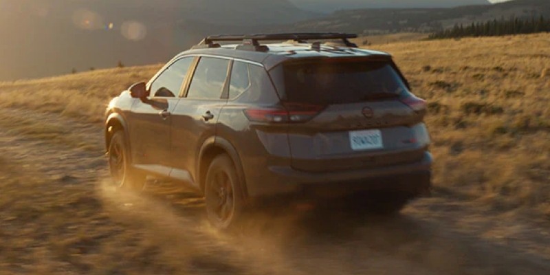 A 2025 Nissan Rogue driving through a dusty, off-road trail, with the sun setting behind the rugged terrain.